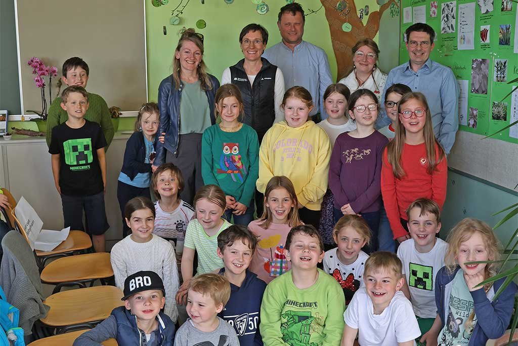 Das Grüne Zimmer von Lindberg Die Grundschule Lindberg hat die Natur in den Klassenraum geholt: Als Nationalpark-Partnerschule verfügt sie nun über eine neue Attraktion – das „Grüne Zimmer“. Die Wände sind in verschiedenen Grüntönen gestaltet, dazu gibt es zahlreiche Informationen zum Nationalpark vor der Haustür sowie zur Natur rund um die Partnerschule in El Salvador, wo ebenfalls ein Nationalpark liegt. Besonders: Alle Schülerinnen und Schüler waren an der Gestaltung beteiligt. „Für die Kinder sind die Programme im Nationalpark immer ein Highlight“, sagte Schulleiter Ralph Bettermann. „Da haben wir uns gedacht, holen wir den Nationalpark noch stärker zu uns.“ Ausgehend von der bereits bestehenden Nationalpark-Ecke entstand so die Idee des Grünen Zimmers. Dank viel Eigenleistung und Unterstützung durch Schüler, Gemeinde, Eltern und Nationalpark wurde sie umgesetzt. „Entstanden ist ein vielseitig nutzbarer Raum, besonders für die Nachmittagsbetreuung.“ „Uns war wichtig, dass jedes Kind im Raum vertreten ist“, erklärte Melanie Klimm, Leiterin der Offenen Ganztagsschule. So entstanden etwa Baumscheiben mit grünen Spiralen. Ergänzt wird der Raum durch echte Pflanzen aus El Salvador und dem Bayerischen Wald, Fühlboxen, tierische Pfotenabdrücke an den Wänden und Pflanzensteckbriefe. „Es ist wirklich etwas ganz Besonderes geworden“, so Klimm. Auch Nationalparkleiterin Ursula Schuster zeigte sich begeistert: „Man merkt, das ist eine gelebte Kooperation. Wenn Kinder Freude daran haben, Wissen zu entdecken und kreativ zu werden, haben wir alles richtig gemacht.“ Bürgermeister Gerd Lorenz betonte ebenfalls: „Ich bin sehr stolz auf unsere Schule. Der Raum bietet eine hervorragende Möglichkeit, Umweltbildung erlebbar zu machen.“ Bild: Während die Ehrengäste nur zur Eröffnung kamen, dürfen die Grundschüler nun öfter im Grünen Zimmer Platz nehmen. (Foto: Gregor Wolf /Nationalpark Bayerischer Wald)